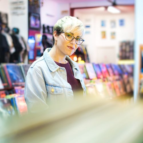 Young Woman Choosing Vintage Vinyl LP In Records Shop Young Woman Browsing Through Vintage Discs and Choosing Vinyl LP In Records Shop. Portrait of Customer Smiling At Camera And Buying Music Albums.